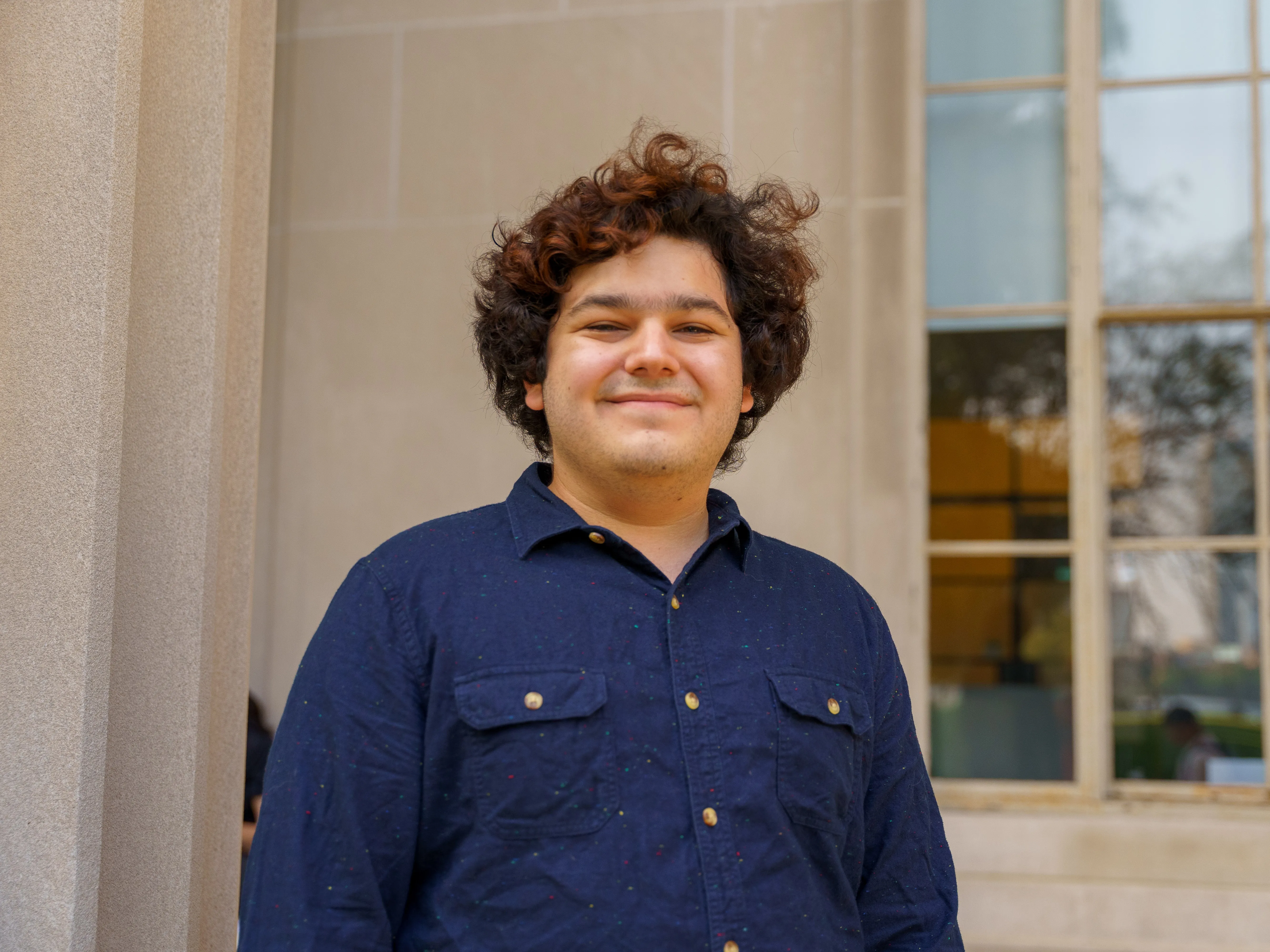 Diego Temkin smiling in a blue button-down shirt in front of a marble column
